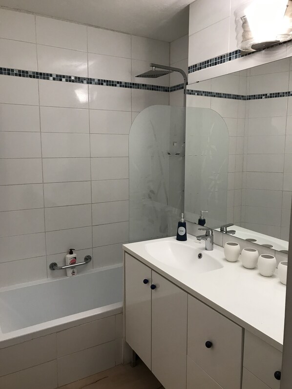 A bathroom with a bathtub, a sink with a mirror, and toiletries.
