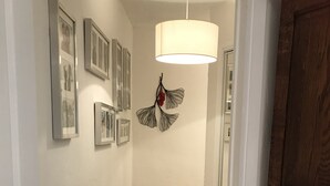 A hallway with framed pictures on the wall, a hanging metal leaf decoration, and a wooden door.