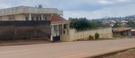 A road with a building on the left and a small structure with a gate.