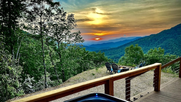 Un jacuzzi en una terraza de madera con vista a la puesta de sol sobre una cordillera boscosa.