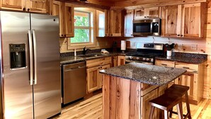 Una cocina con armarios de madera, electrodomésticos de acero inoxidable, encimeras de granito y un ventanal con vistas a la vegetación.