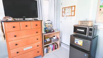 A room with a television on a dresser, a refrigerator, a bookshelf, and a bed with a floral bedspread.