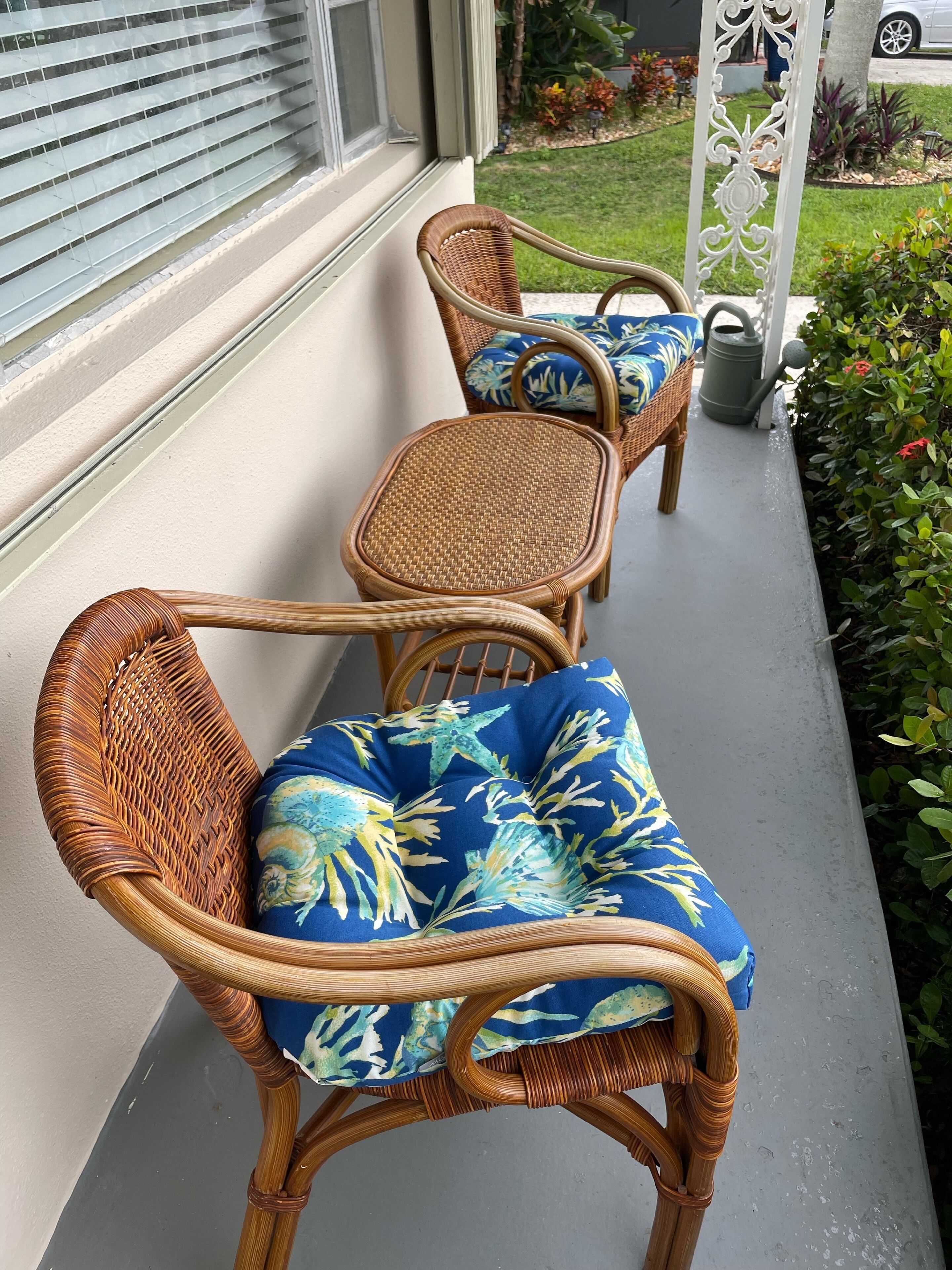 Korbstühle mit blau blumigen Kissen auf einer Betonterrasse.