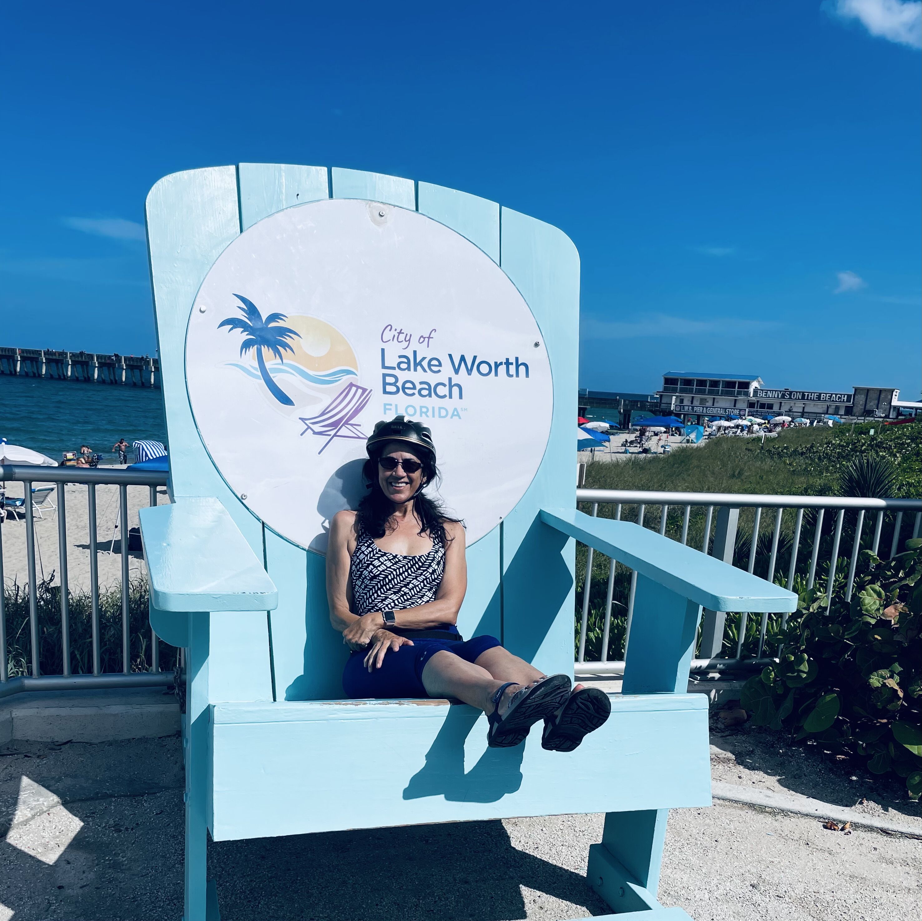 Een persoon zittend op een lichtblauwe stoel, met op de achtergrond een bord waarop 'City of Lake Worth Beach, Florida' staat.