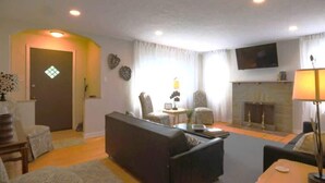 Ein Wohnzimmer mit einer Couch, Sesseln, einem Kamin und einem Fernseher.