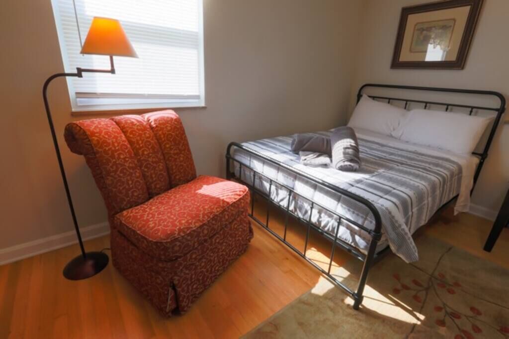 Un dormitorio pequeño con una cama individual, una silla y una lámpara de pie.