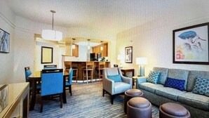 A hotel room with a living area featuring a sofa, ottomans, and a dining area with chairs and a table. - Marriott Cypress Harbour resort (Orlando)