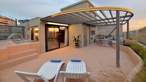 En modern uteplats med en välvd pergola, en entré med glasdörr och en sittgrupp med bord och stolar.