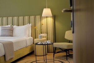 Una camera d'albergo con un letto, un comodino con una lampada, una sedia e un tavolino rotondo con un vassoio.