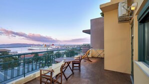 A balcony with a view of a river and a cruise ship. There are two wooden chairs and a table.