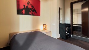 A hotel room with a bed, a nightstand, a lamp, a wardrobe, and a red artwork on the wall.