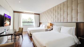 A hotel room with two beds, a desk, a chair, a TV, and a window with curtains.