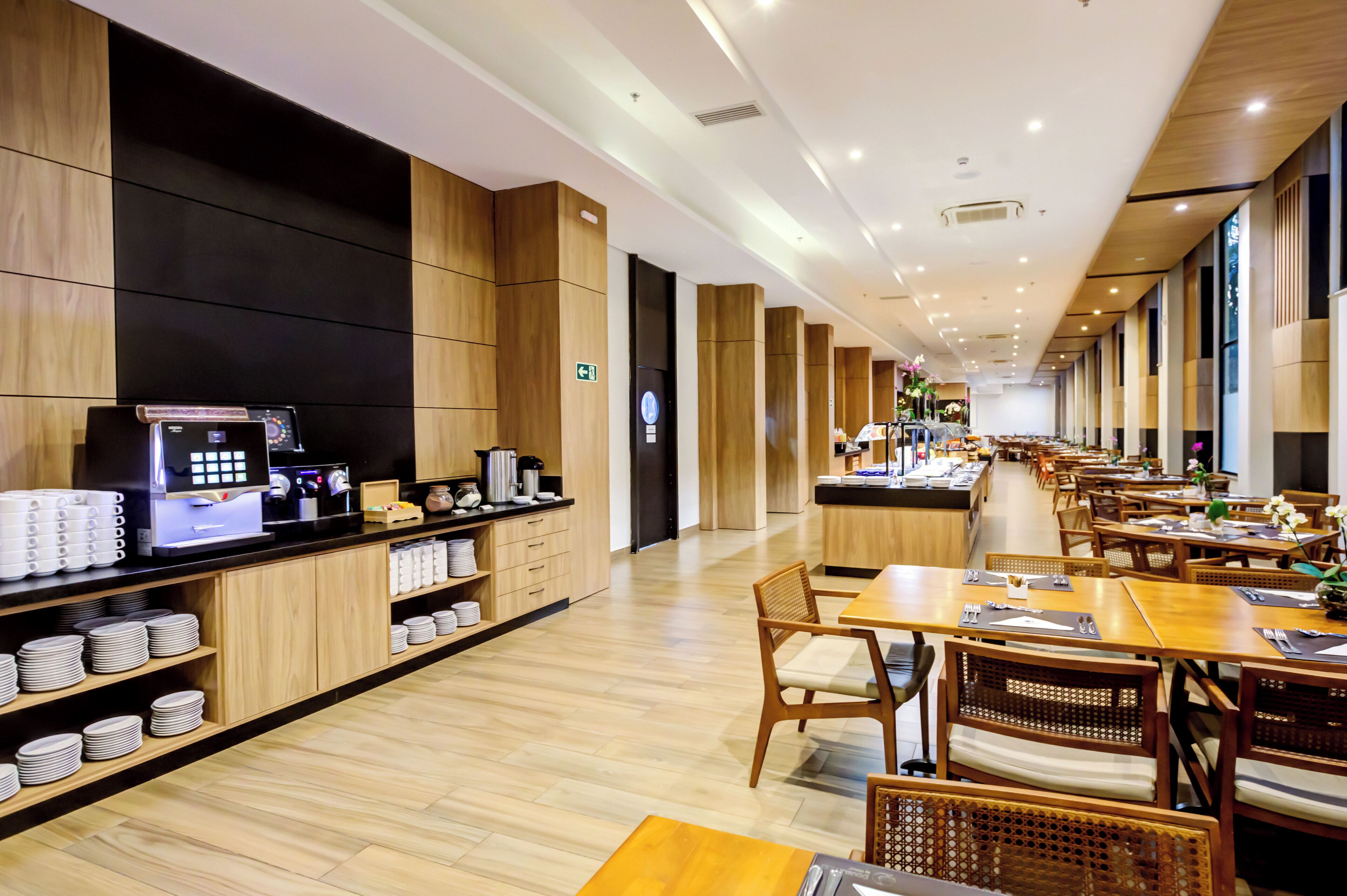 Un hall d’hôtel moderne avec des panneaux de bois, un kiosque en libre-service, ainsi que des tables et des chaises disposées de manière ordonnée.