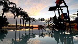 Vista da piscina com palmeiras e pôr do sol.