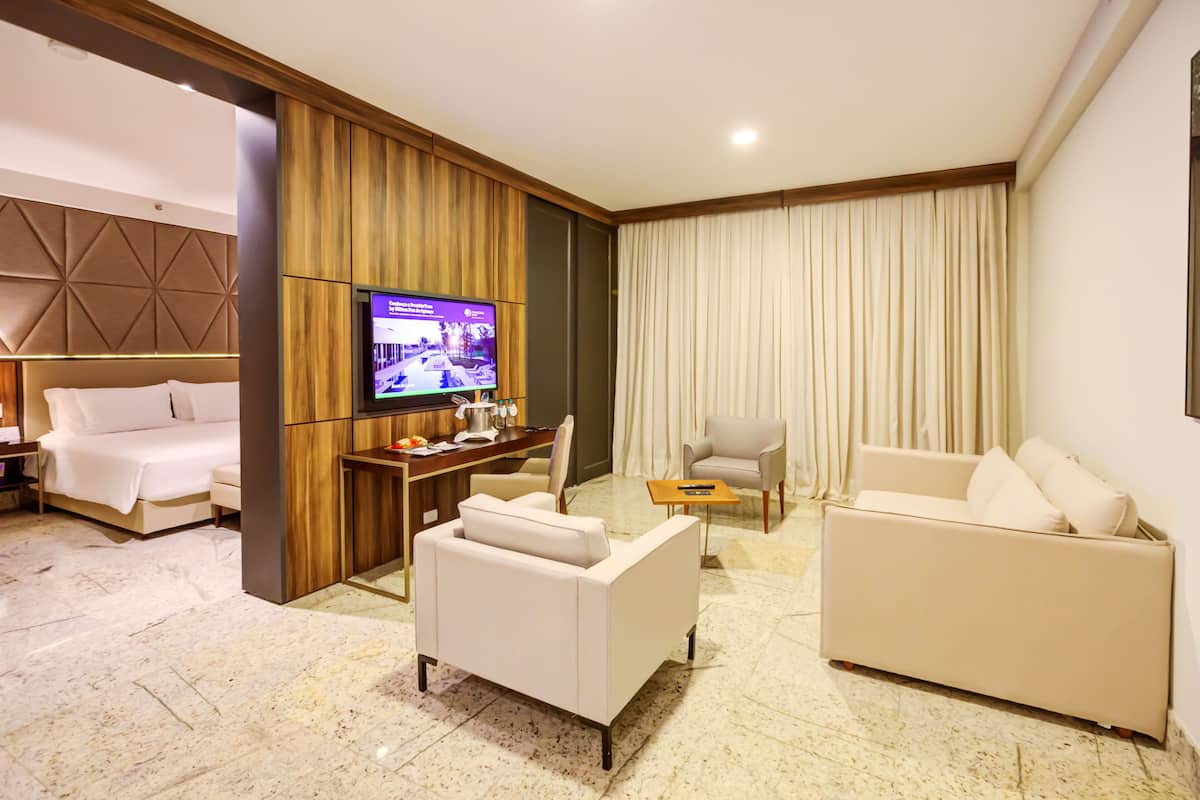 A modern hotel room with a large flat-screen TV, a sofa, a chair, and a bed.