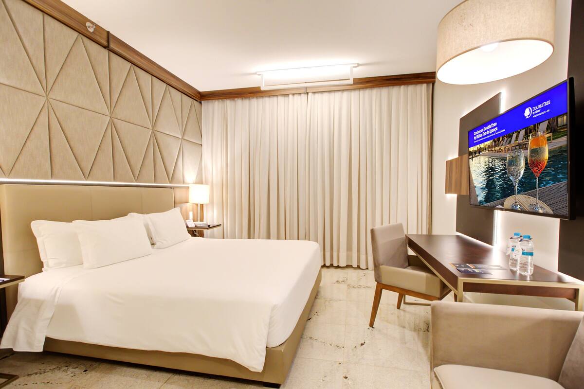 A hotel room with a large bed, a desk with two chairs, a TV on the wall, and a curtain.