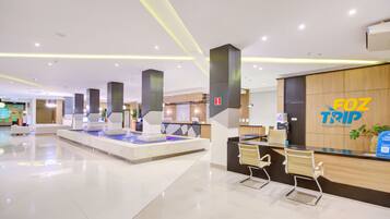 A modern hotel lobby with a reception desk, seating area, and a water feature.