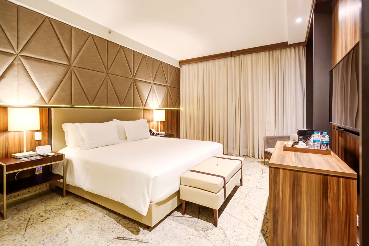 A hotel room with a large bed, bedside tables, a desk with a chair, and a TV.