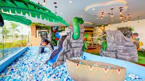 Área de recreação infantil com piscina de bolinhas, escorregadores e uma grande escultura de cobra verde.