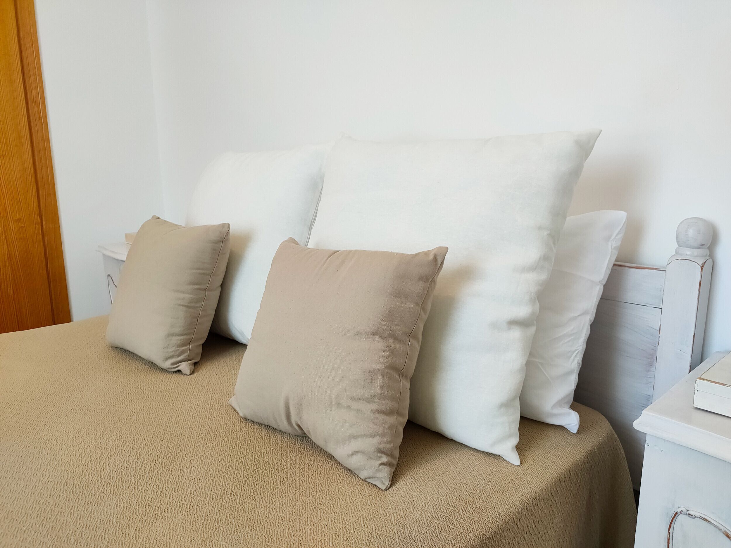 A bed with a beige cover, two pillows, and a white headboard.