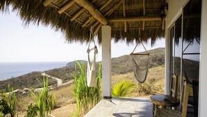Un patio con techo de paja, una hamaca y vistas al océano.