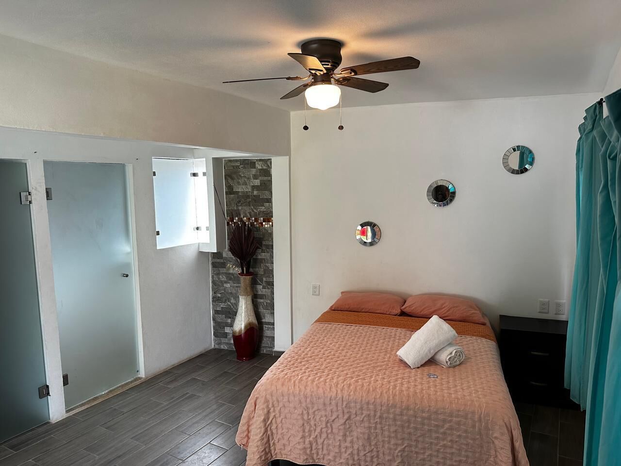 A bedroom with a bed, a ceiling fan, a vase, and a mirror on the wall.