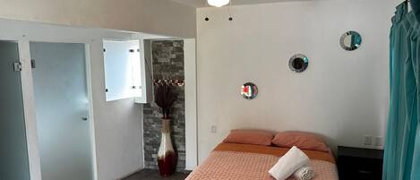 A bedroom with a bed, a ceiling fan, a vase, and a mirror on the wall.