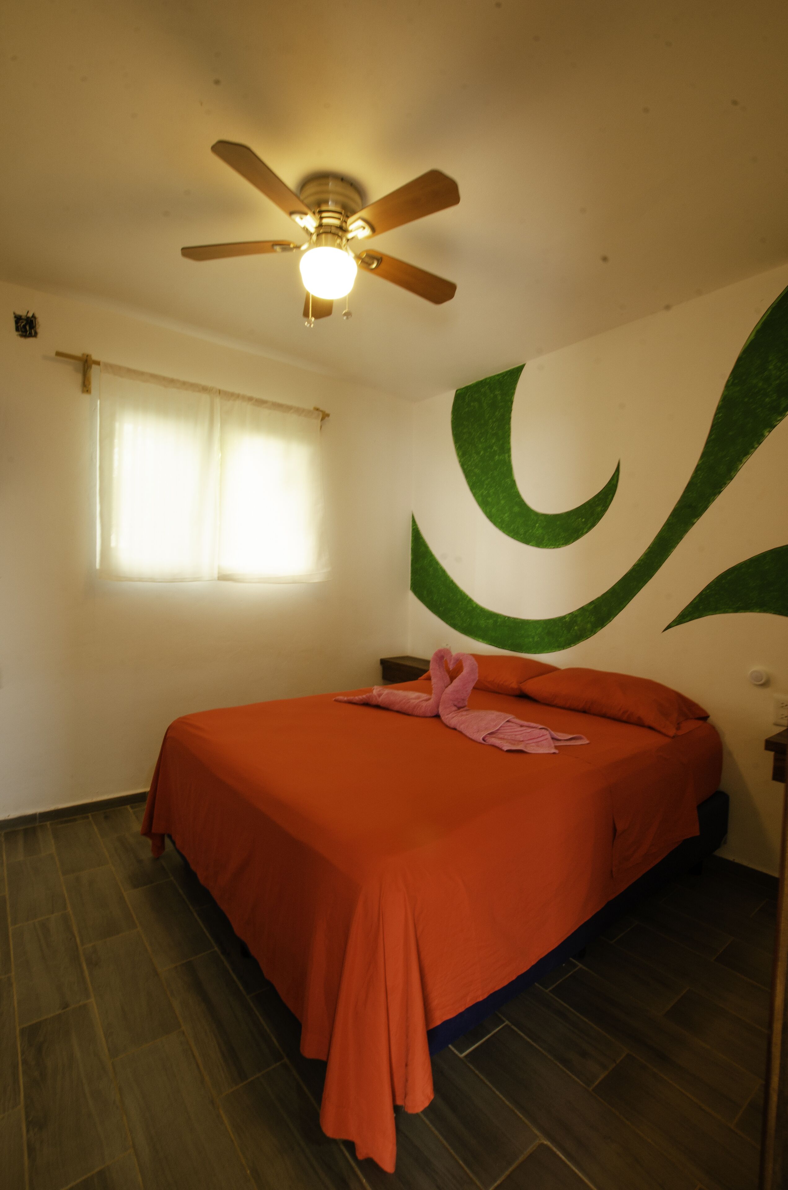 A bedroom with a bed, a ceiling fan, a window with curtains, and a wall with a green design.