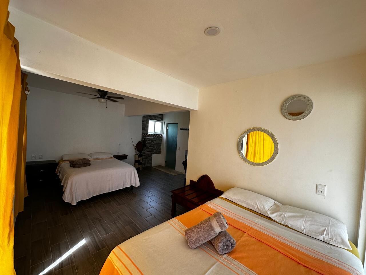 Ein Hotelzimmer mit zwei Betten, einem kleinen Tisch, einem Spiegel und einem Deckenventilator.