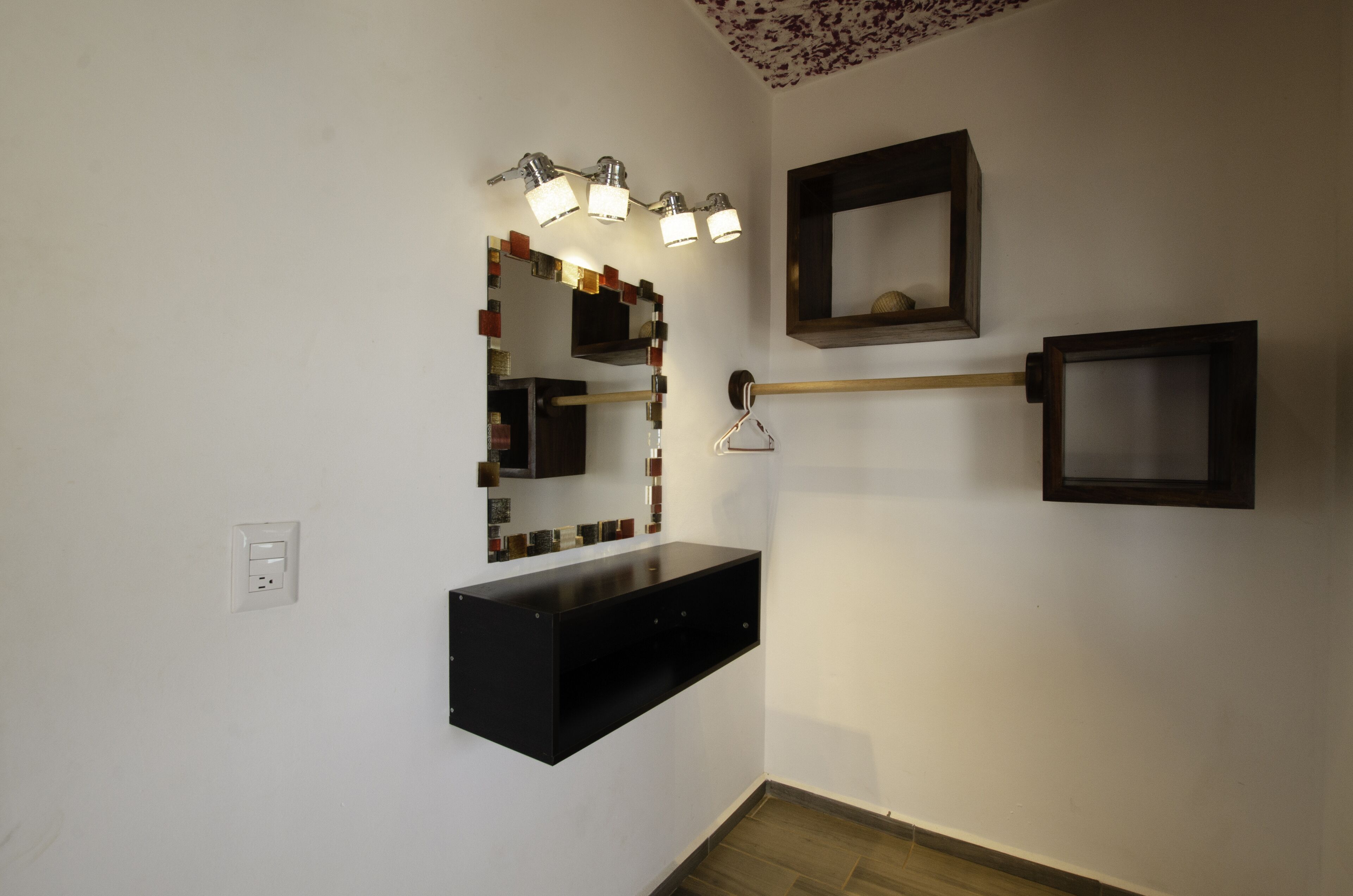 Un baño con tocador, espejo con iluminación, estante y armario de pared.