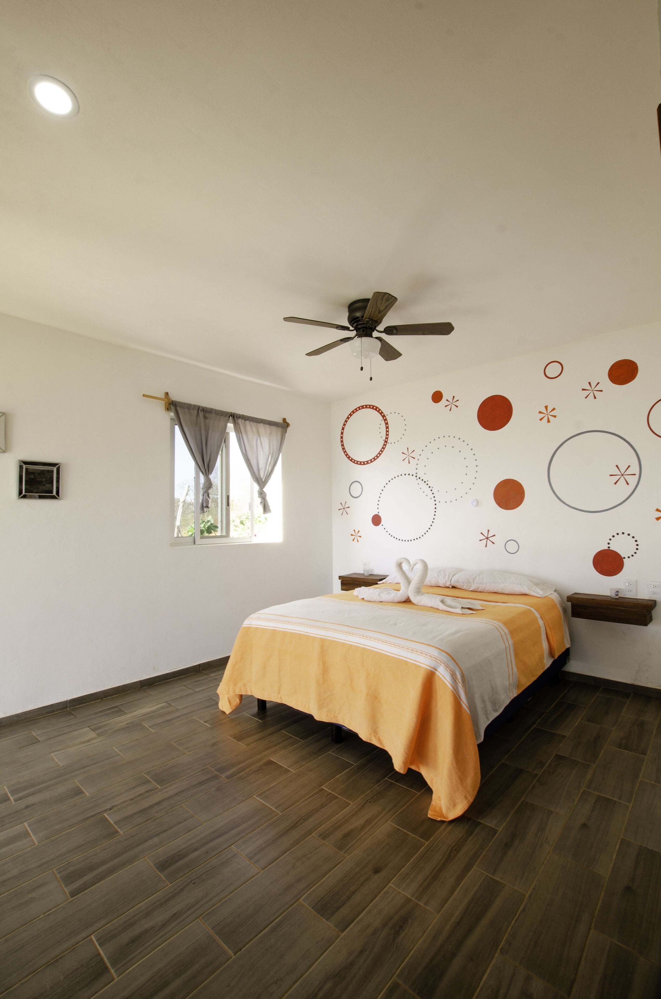 Un dormitorio con cama, ventilador de techo, ventana con cortinas y decoración en las paredes.