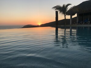 A serene sunset over a calm pool with palm trees and lounge chairs. - Villas del Sol (Villa del Mar)