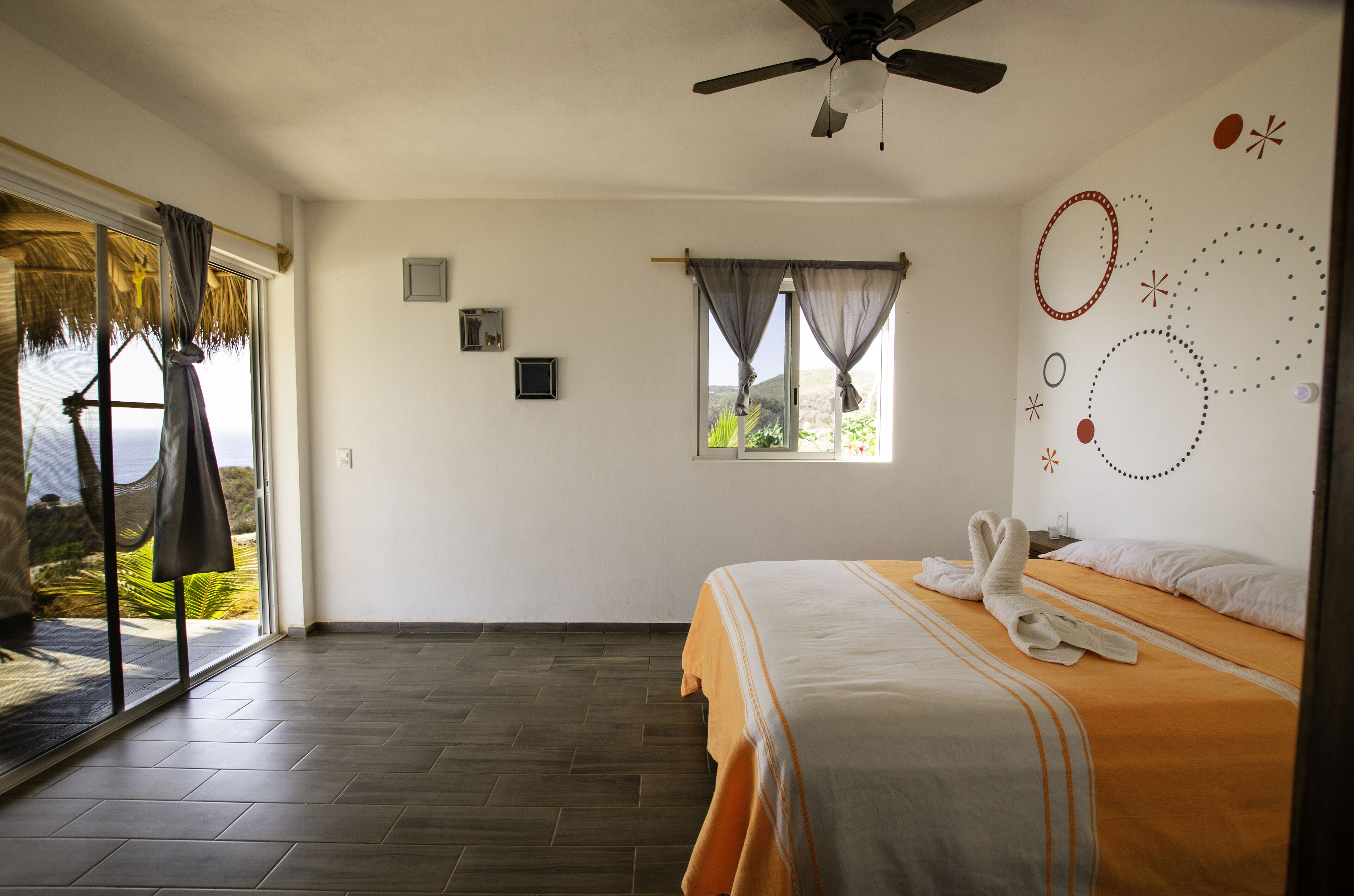 A bedroom with a bed, a ceiling fan, a window with curtains, and a view of the outdoors.