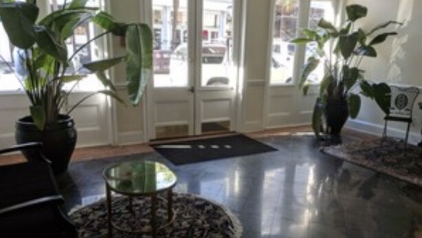 A lobby with a glass coffee table, two potted plants, a black rug, and a bench.
