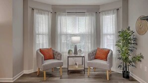 A living room with two grey armchairs, a small table with a lamp, and a large window with blinds. - CHAS, SUMMRVLL/NEXTON Comfort  Near Everything! (Summerville)