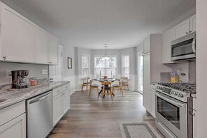 A modern kitchen with white cabinets, a central island with chairs, a built-in oven, and a large window.