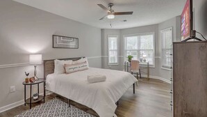 A bedroom with a bed, a ceiling fan, a nightstand, a lamp, a framed picture, and a window with blinds. - CHAS, SUMMRVLL/NEXTON Comfort  Near Everything! (Summerville)