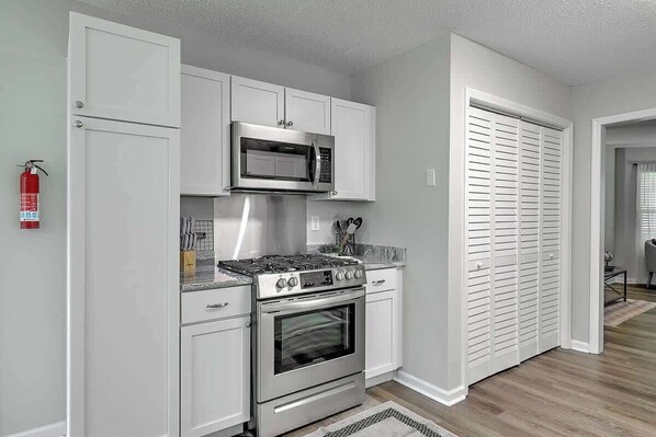 A compact kitchen with white cabinetry, a stainless steel stove, and a microwave.
