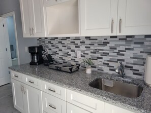 A modern kitchen with white cabinetry, a granite countertop, a coffee maker, and a small plant. - A cheerful and cozy place (Tampa)