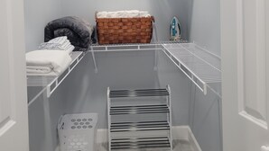 Ein kleiner, begehbarer Kleiderschrank mit Regalen aus Metall, einem Wäscheständer und einem Wäschekorb.