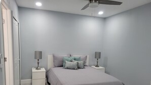 Ein Schlafzimmer mit einem Bett, zwei Nachttischen, einem Deckenventilator und einer Tür.