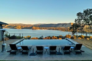 Une piscine entourée de chaises longues et de tables, avec vue sur un lac et des montagnes.