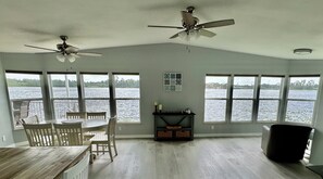 Una habitación con una mesa de comedor y sillas, un ventilador de techo y grandes ventanas con vistas al agua.