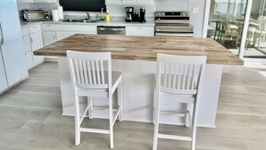 A modern kitchen with white cabinets, a wooden island, and two white bar-style chairs.