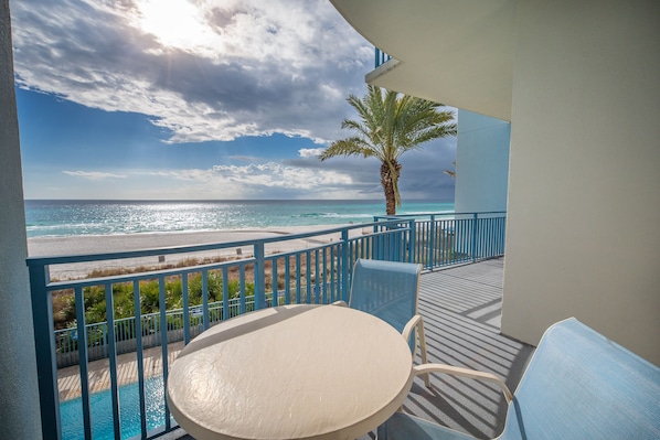Ein Balkon mit Blick auf den Ozean und den Strand, eine Palme und ein Pool.