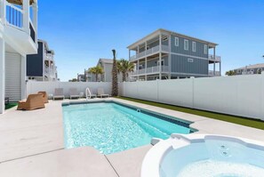 A swimming pool with lounge chairs, a hot tub, and a two-story building in the background.