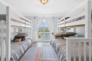 A room with bunk beds, a large window with curtains, and a view of the outside.