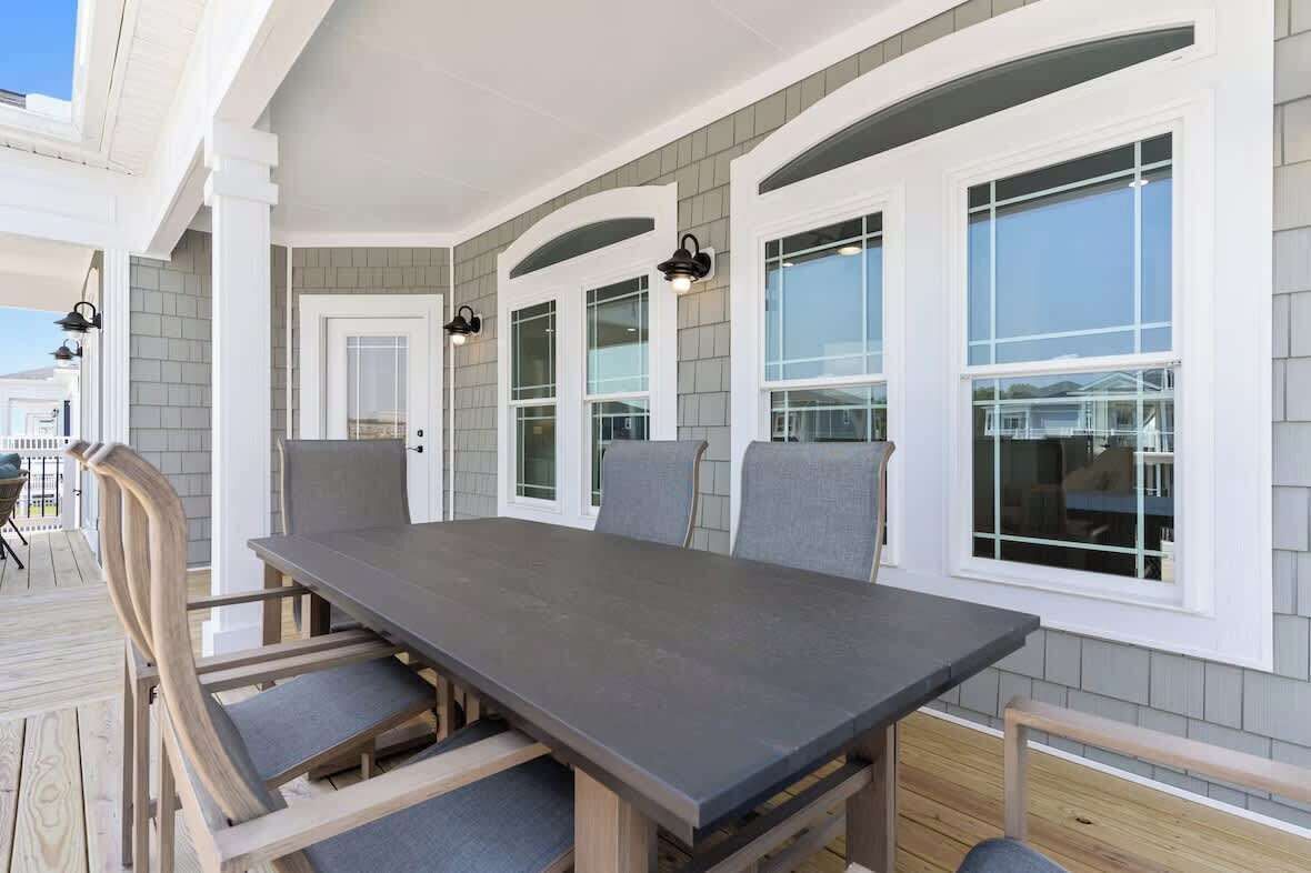 Un patio techado con una mesa larga y sillas, ventanas amplias y una puerta.