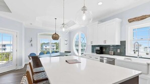 A modern kitchen with a large island, white cabinetry, and pendant lighting. - Beach Please! (Ocean Isle Beach)