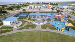 A playground with slides and climbing structures, surrounded by a landscaped area with palm trees and a covered pavilion. - Beach Please! (Ocean Isle Beach)